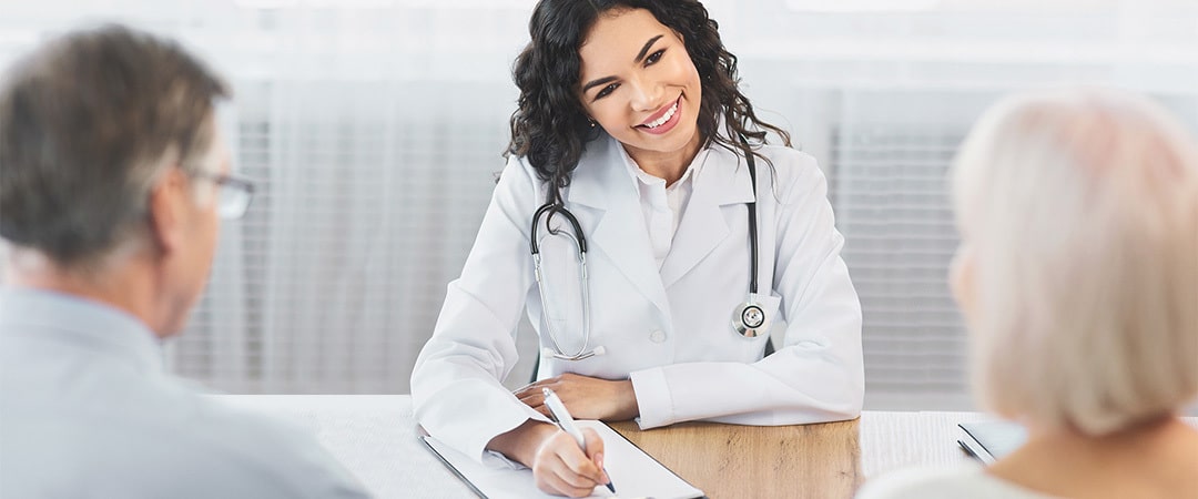 A doctor sitting with two seniors at a table going over paperwork on a clipboard.